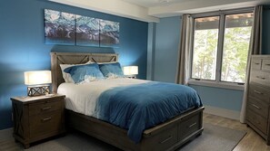 Ein Schlafzimmer mit einem Bett, Nachttischen, einer Kommode und einem Fenster mit Vorhängen.