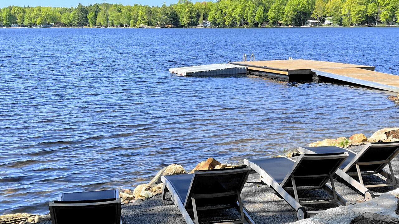 A lakeside setting with a dock extending into the water, surrounded by lounge chairs and a concrete edge.