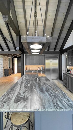 Une cuisine moderne dotée d’un grand îlot central, d’appareils électroménagers en acier inoxydable et d’un luminaire suspendu.
