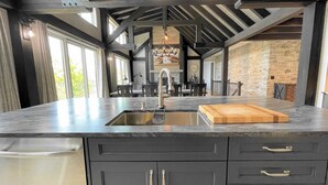 Een moderne keuken met een groot eiland, donkere kastjes en een accentmuur van steen.