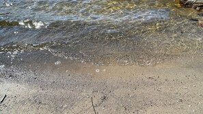Ein sandiger Strand mit klarem Wasser und kleinen Kieselsteinen.