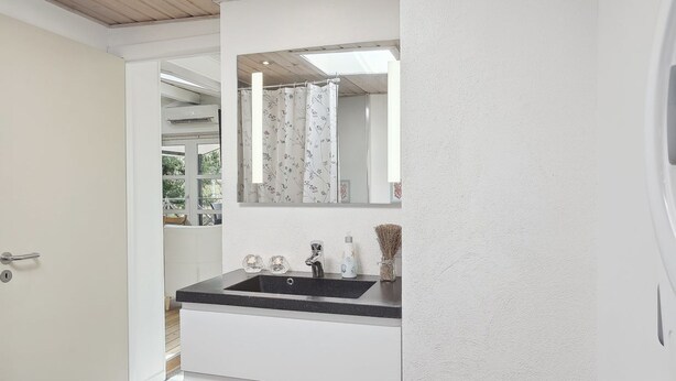 Ein Badezimmer mit einem weißen Waschbecken, einem Spiegel und einem Fenster mit blumigem Vorhang.