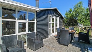 A wooden deck with wicker furniture, a chimney, and a large window overlooking a garden.