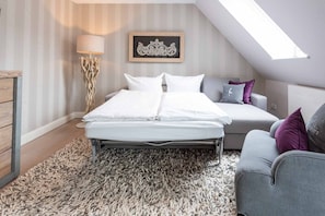 Een slaapkamer met een bed, een slaapbank, een vloerlamp en een kunstwerk aan de muur.