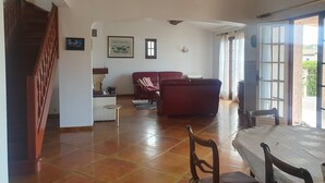 Ein geräumiger Wohnbereich mit einem roten Sofa, einem Esstisch mit Stühlen, einer Treppe und Blick durch eine Glastür ins Freie.