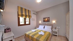 Une chambre à coucher comprenant un lit, une table de chevet, une commode, une fenêtre avec un rideau à rayures, un climatiseur et un tableau accroché au mur.