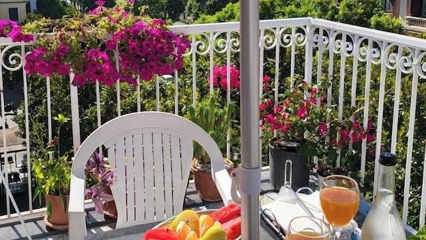 A table set with fruits, glasses, and a bottle on a balcony with a view of the sea and buildings. - Divina Salerno (Salerno)