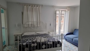 A bedroom with a bed, a nightstand, a window with curtains, and a blue sofa. - Divina Salerno (Salerno)