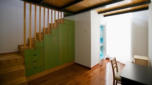 A room with a wooden staircase, green cabinets, a dining table, and a view of a blue sky through a window. - Divina Salerno (Salerno)