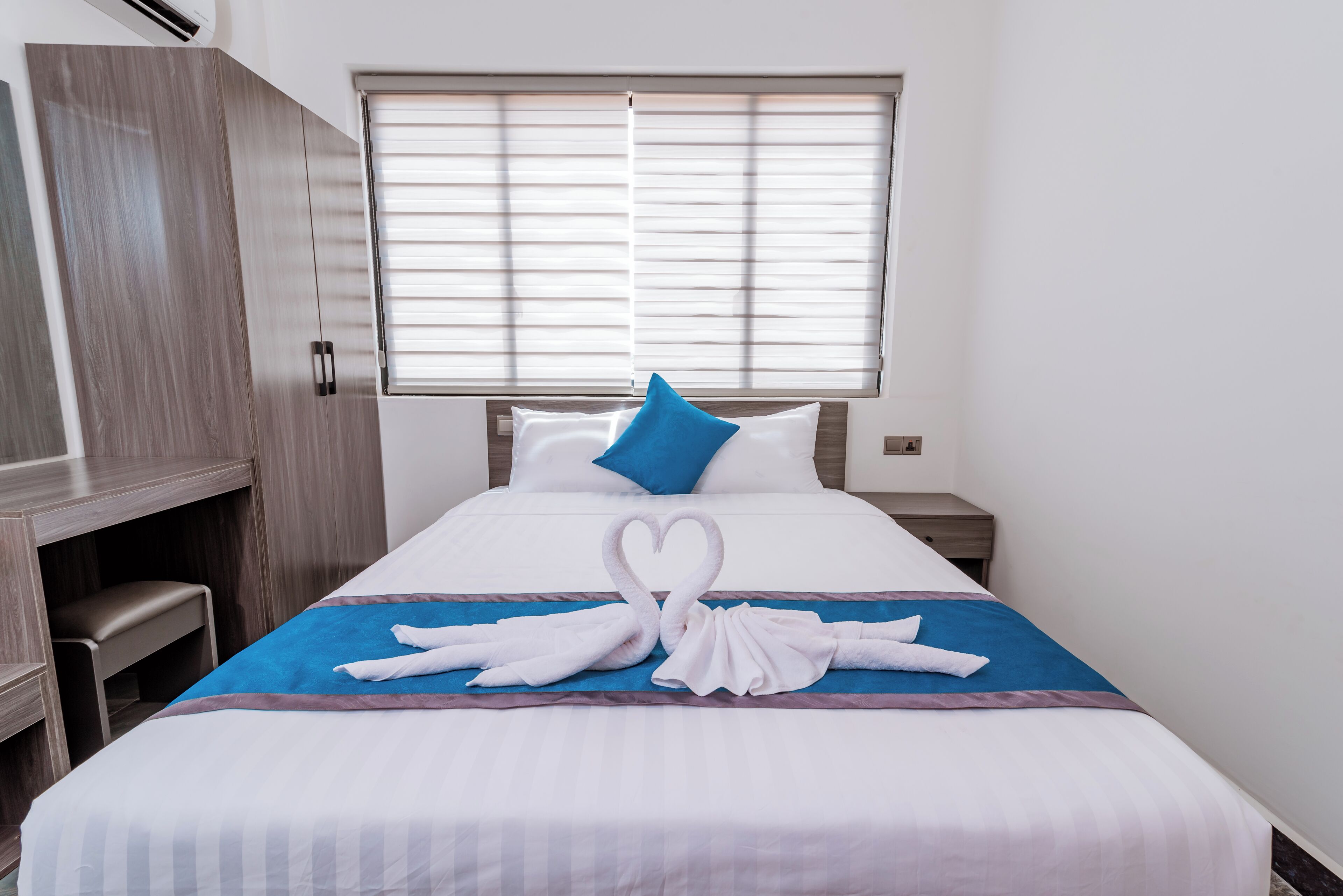 A hotel room with a bed, a desk, and a window with blinds.