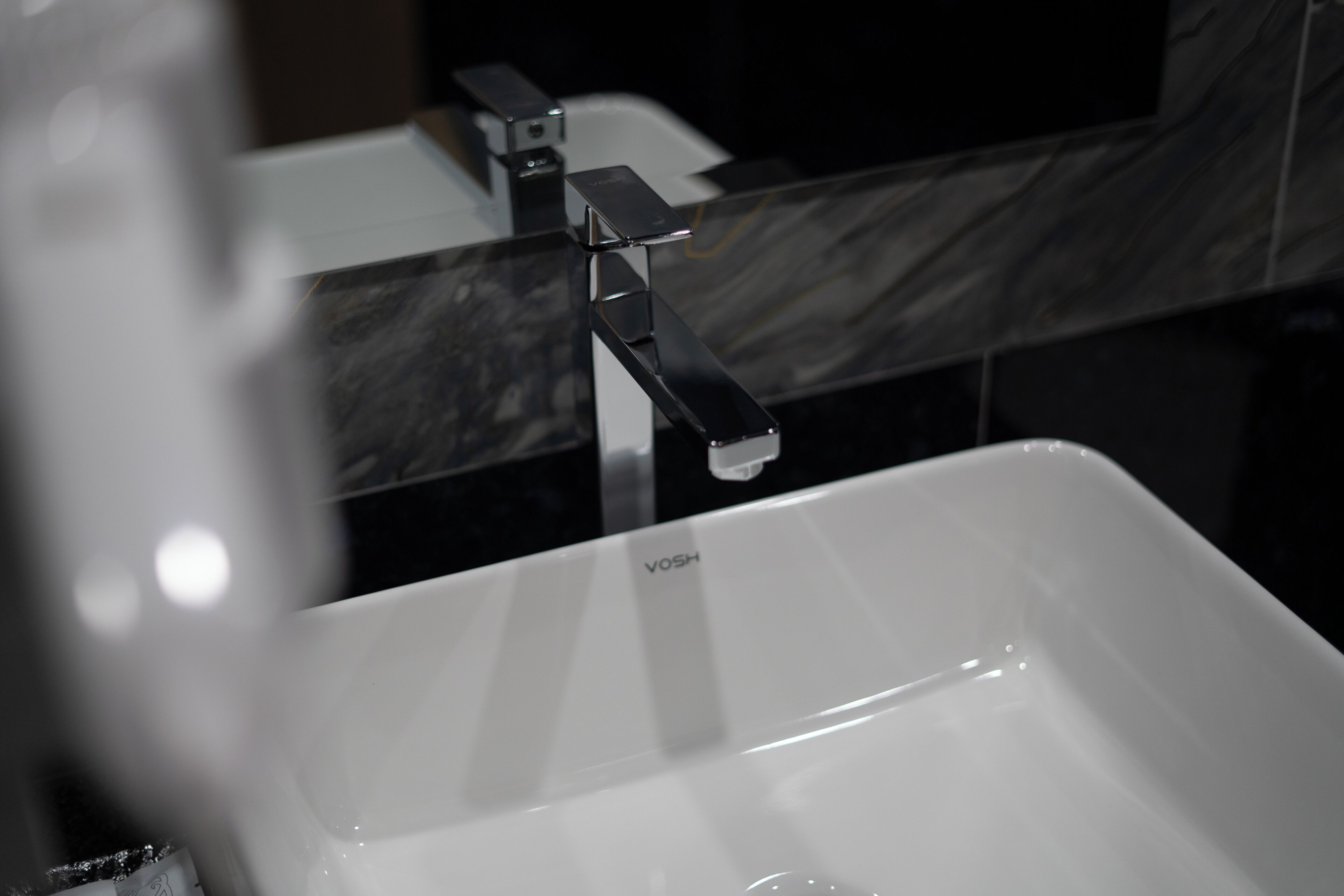 Un baño moderno con un lavamanos blanco, un grifo negro y una encimera de mármol.