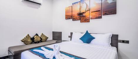A hotel room with a bed, a wall-mounted air conditioner, and a set of three paintings depicting a sunset over the sea.