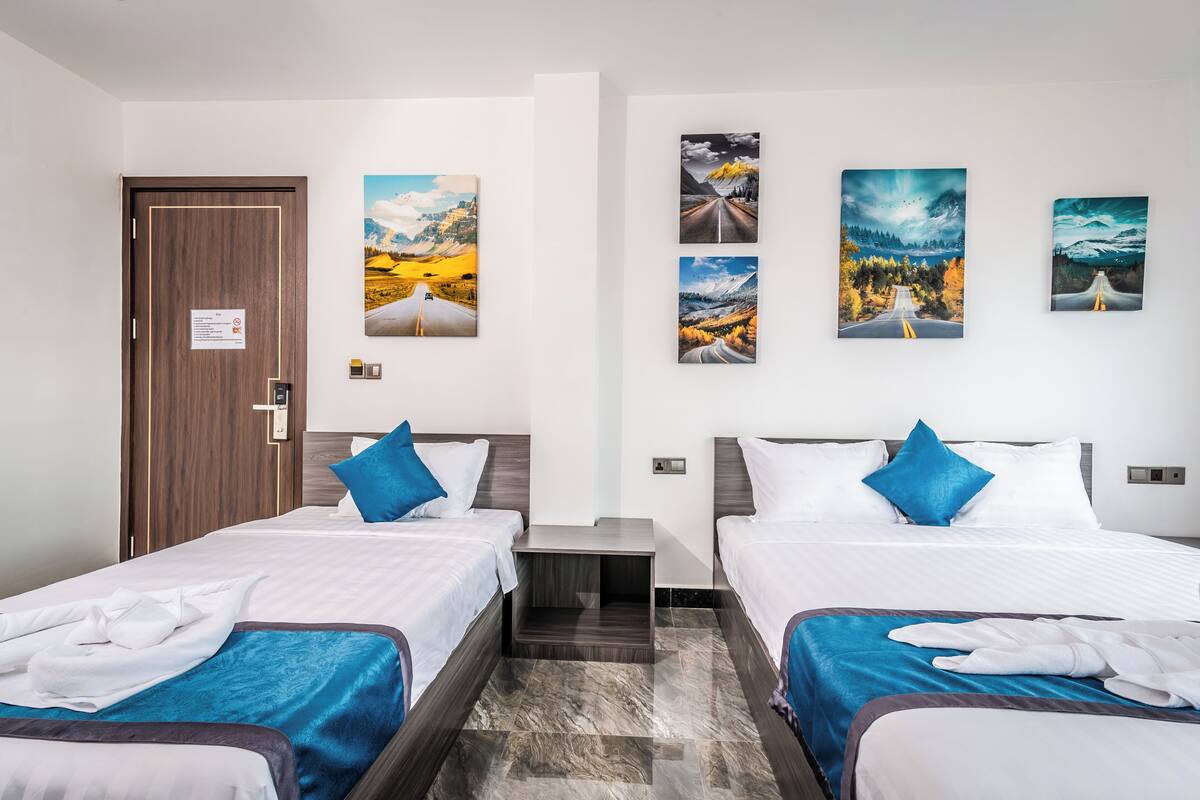 A hotel room with two beds, a wooden door, and four paintings on the wall.