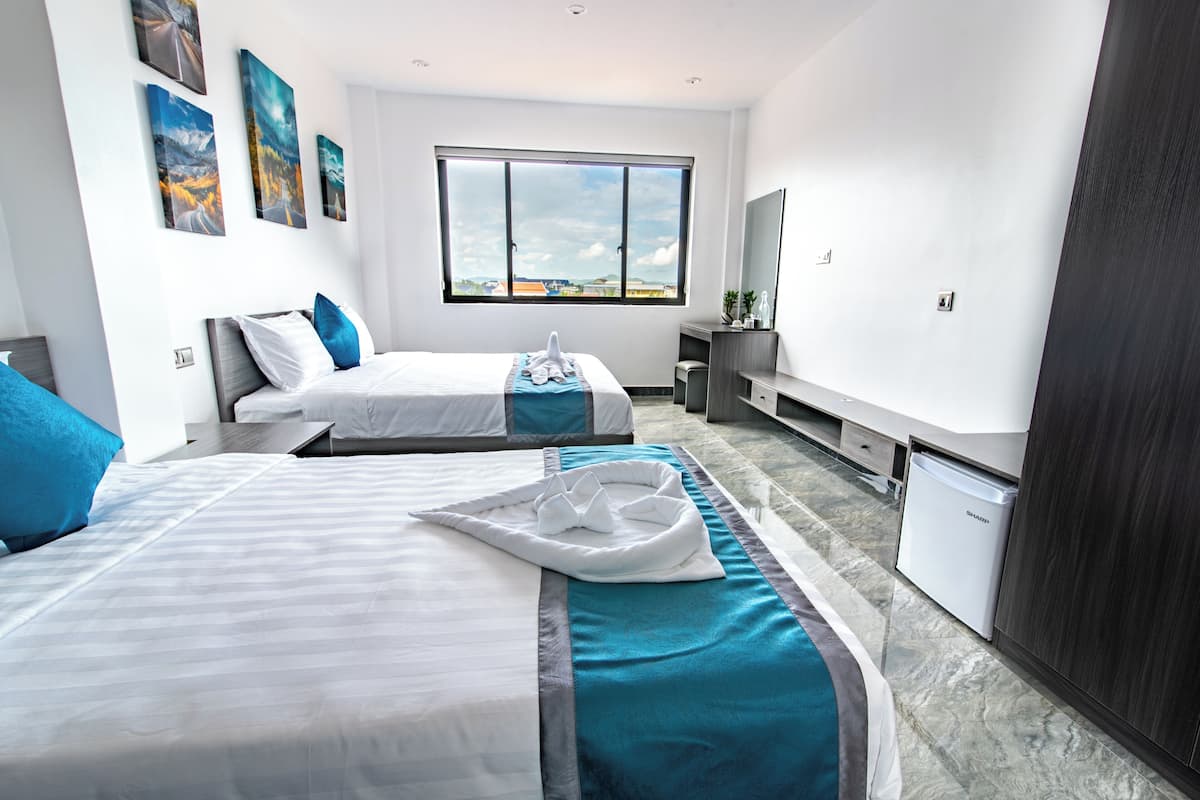 A modern hotel room with two beds, a large window, a minibar, and a view of the city.
