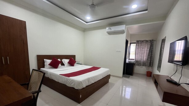 A hotel room with a bed, a desk, a chair, an air conditioning unit, a television, and a bathroom visible through an open door. - Shelke Mama's Lodging & Resorts (Chhatrapati Sambhajinagar)