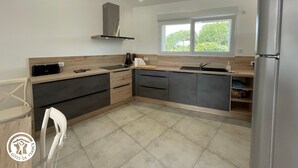 A modern kitchen with a stainless steel refrigerator, a window with a view of greenery, and a built-in oven. - Cozy Cottage for 6 with Terrace – Near La Faute sur Mer & Puy du Fou (Les Magnils-Reigniers)