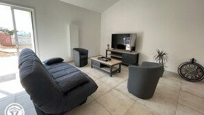 A modern living room with a sofa, armchair, TV stand, and a clock on the wall. - Cozy Cottage for 6 with Terrace – Near La Faute sur Mer & Puy du Fou (Les Magnils-Reigniers)