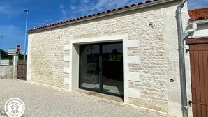 A stone building with a tiled roof, a glass door entrance, and a metal gate. - Cozy Cottage for 6 with Terrace – Near La Faute sur Mer & Puy du Fou (Les Magnils-Reigniers)