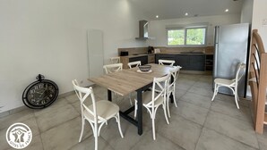A modern kitchen with a dining area, featuring a wooden table, white chairs, and a stainless steel refrigerator. - Cozy Cottage for 6 with Terrace – Near La Faute sur Mer & Puy du Fou (Les Magnils-Reigniers)