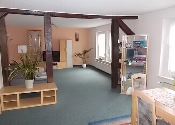 A room with a green carpet, wooden furniture, a potted plant, and a window.