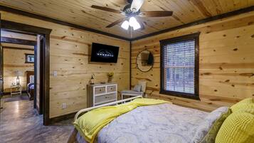 Een slaapkamer met houten lambrisering, een bed, een plafondventilator, een televisie, een raam met zonwering en een klein tafeltje met een lamp.