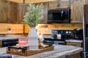 A kitchen with wooden cabinets, a microwave, a coffee maker, a vase with green plants, and a tray with a glass and a candle.