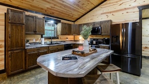 Una cocina con armarios de madera, encimera de mármol, refrigerador de acero inoxidable y techo de madera.