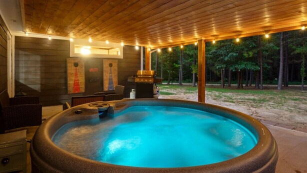 Un jacuzzi con terraza de madera y luces colgantes, rodeado de zona boscosa.