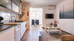 Une cuisine moderne équipée d’une cuisinière intégrée, un coin repas avec une table et des chaises, un canapé et un téléviseur fixé au mur.