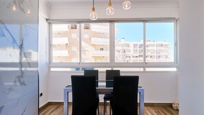 Un espace repas comprenant une table et des chaises, de grandes fenêtres offrant une vue sur les bâtiments et un luminaire moderne.