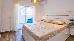 Une chambre avec un grand lit, une table de chevet, une lampe et une vue sur l’extérieur.