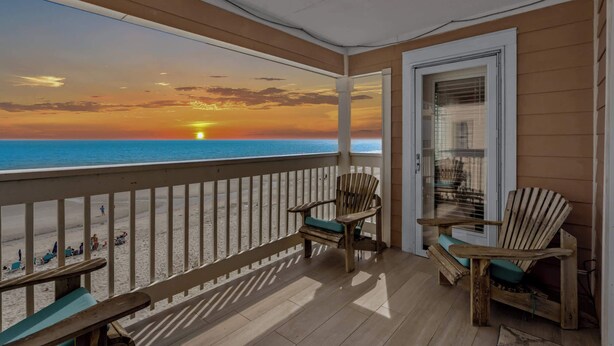 A wooden deck with a view of the sunset over the ocean, two wooden chairs, and a table. - Duneside Unit 302 - Oceanfront (Murrells Inlet)