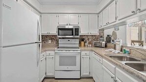 A modern kitchen with white cabinetry, a built-in microwave, stove, and a double sink. - Duneside Unit 302 - Oceanfront (Murrells Inlet)