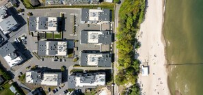 An aerial view of a coastal hotel with multiple buildings, a parking lot, and a beach with people.
