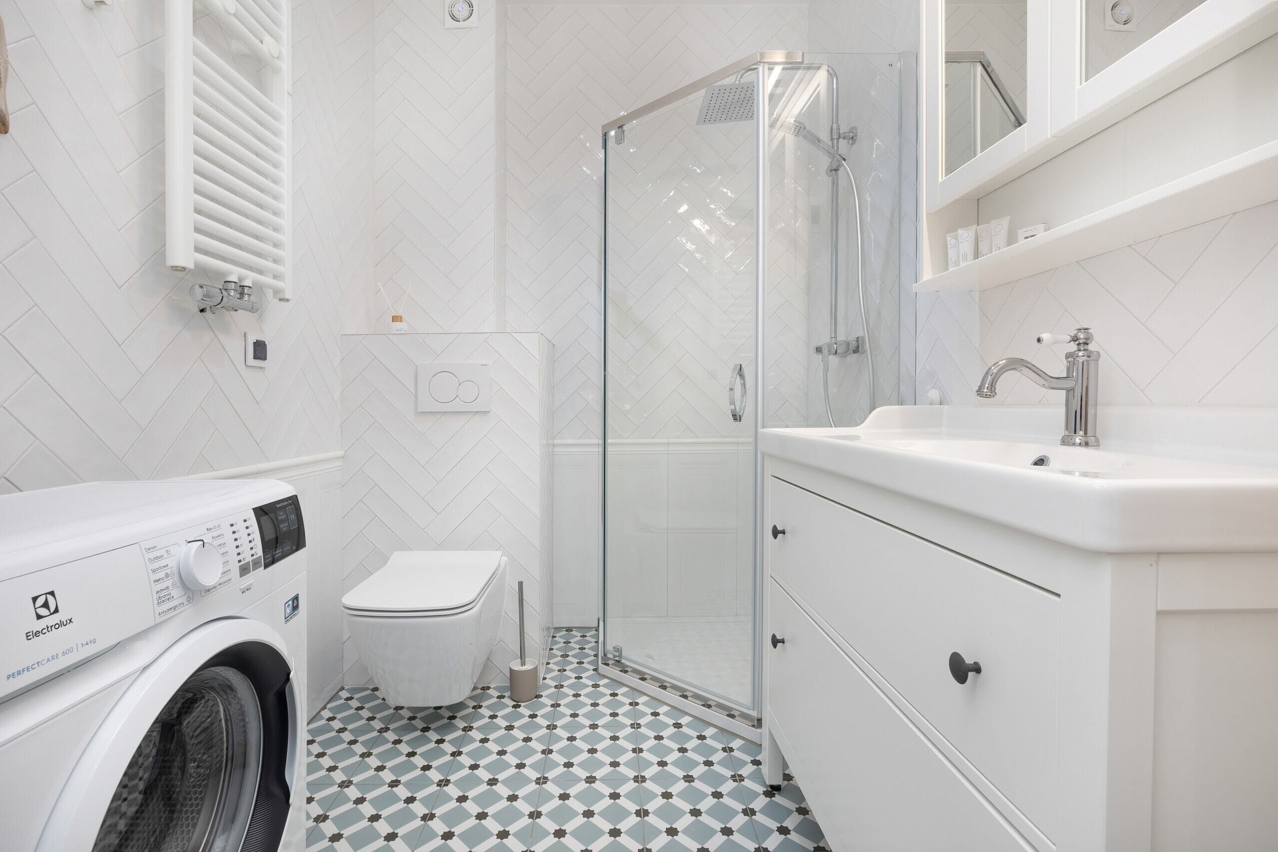 Un baño moderno con lavadora, inodoro, cabina de ducha de vidrio y muebles de color blanco.