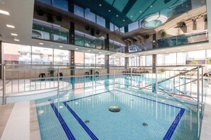 An indoor swimming pool with a tiled floor, surrounded by glass railings and multiple levels with balconies.