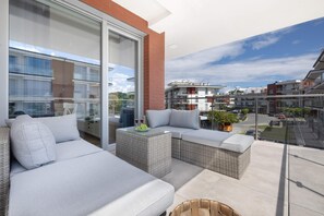 Enjoy a comfortable outdoor seating area with a sofa, wicker chair, and table, offering a clear view of the surrounding urban landscape.