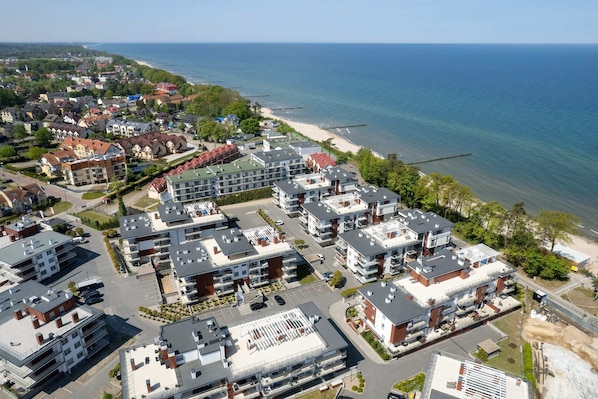 An aerial view of a coastal residential area with modern apartment buildings, a beach, and a clear view of the ocean.