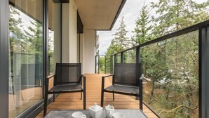 A balcony with a table set for tea, two chairs, and a view of trees and a building.