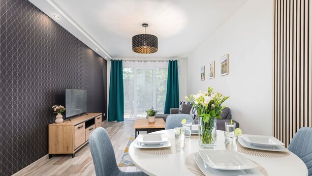 A modern living room with a dining area, featuring a TV, wooden cabinet, and a dining table set with plates and glasses.