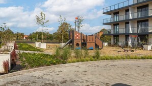 A playground with slides and climbing structures, surrounded by landscaped gardens and a modern building with balconies.
