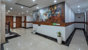 A lobby with a large mural, a staircase, and a fire exit sign. - The Classio By DLS Hotels (Narendranagar)