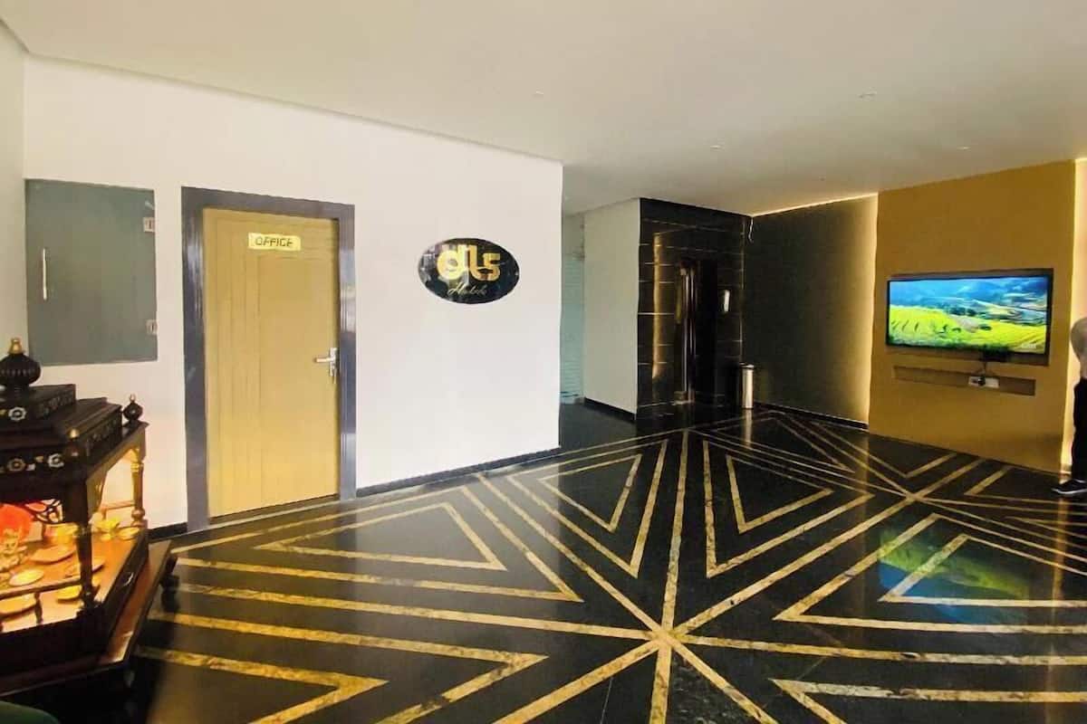 Un hall d’hôtel avec un motif géométrique sur le sol, un comptoir d’accueil, un écran de télévision et une porte portant l’inscription « BUREAU ».