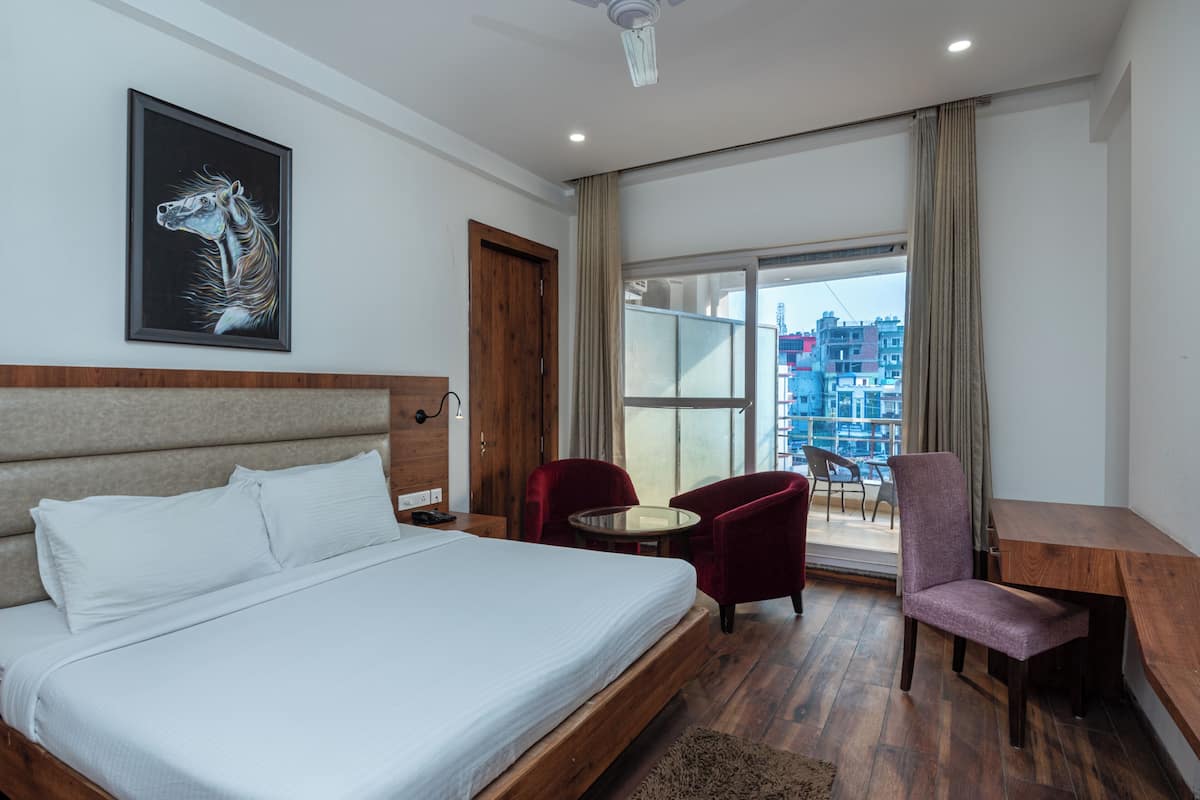 Une chambre d’hôtel avec un lit, un bureau, deux chaises, une grande fenêtre et une vue sur la ville.