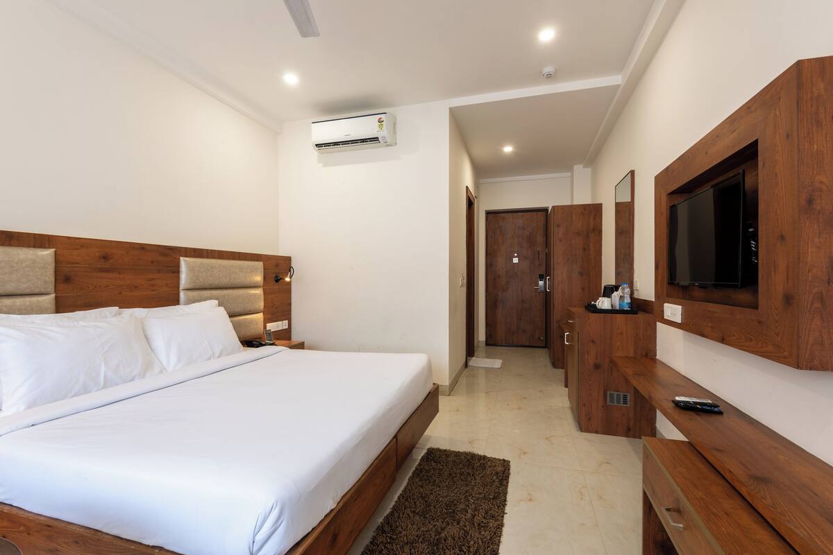 Une chambre d’hôtel moderne dotée d’un grand lit, d’une tête de lit en bois, d’un téléviseur à écran plat, d’une armoire en bois et d’un appareil de climatisation.