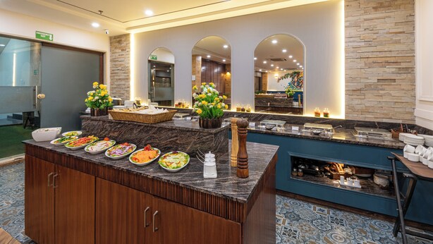 A buffet area with various dishes, a stone wall, and a mirror reflecting the room. - The Classio By DLS Hotels (Narendranagar)