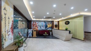 A hotel lobby with a reception desk, a red sofa, a mural on the wall, and a glass partition. - The Classio By DLS Hotels (Narendranagar)