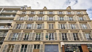 A multi-story building with a row of balconies, a ground-floor shop, and a visible storefront. - JARDIN DU LUXEMBOURG -RUE DE ASSAS -3 BEDROOM WITH AIR CON (paris)