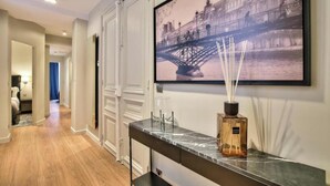 A hallway with a marble console table, a framed picture of a bridge, and a diffuser with reed sticks. - JARDIN DU LUXEMBOURG -RUE DE ASSAS -3 BEDROOM WITH AIR CON (paris)