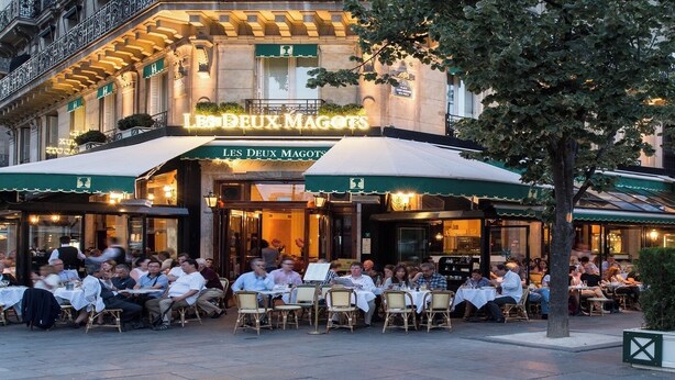 An outdoor dining area of a restaurant with tables and chairs, and a building with a sign reading "LES DEUX MAGOTS". - JARDIN DU LUXEMBOURG -RUE DE ASSAS -3 BEDROOM WITH AIR CON (paris)